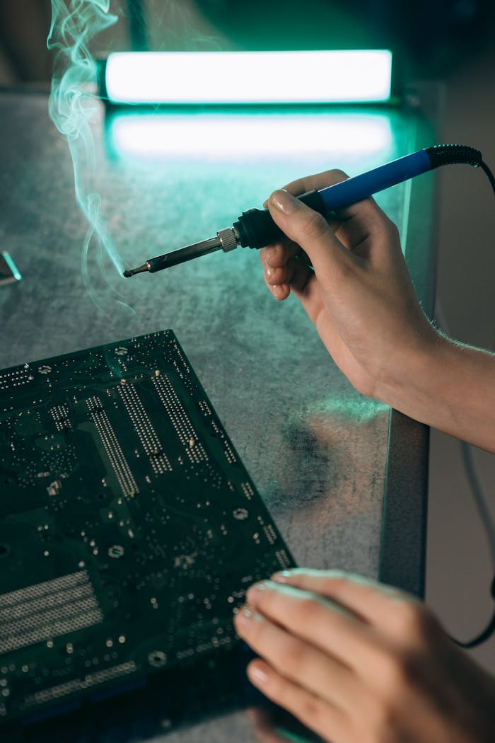Close-up of hands working on a motherboard with a soldering iron, producing smoke.